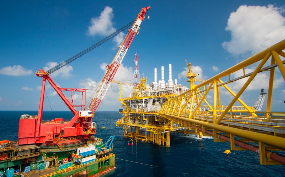An offshore oil platform with crane and drilling equipment in the ocean under a blue sky.